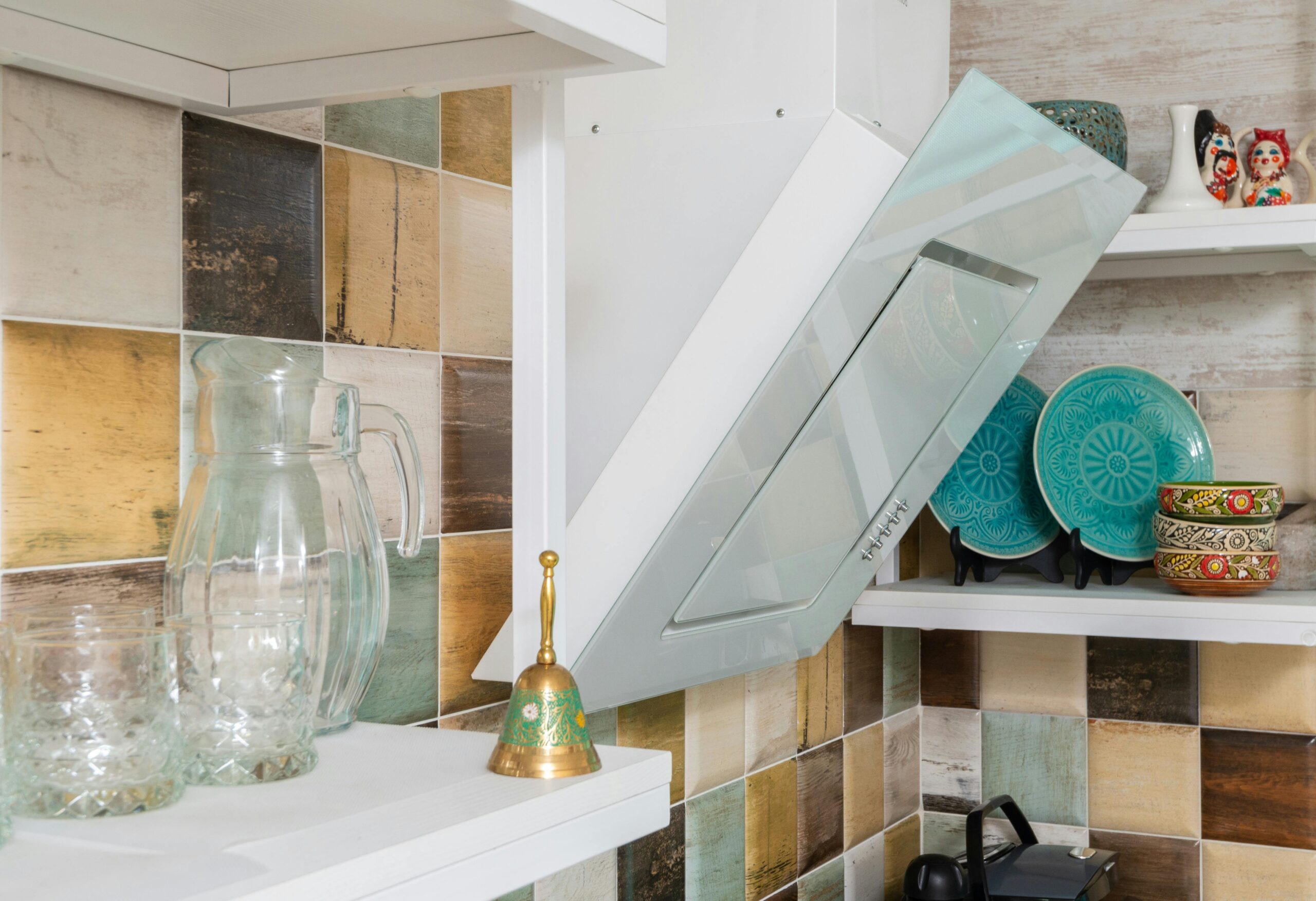 Interior of light kitchen furnished with shelves with various dishware and glass bottles in modern apartment